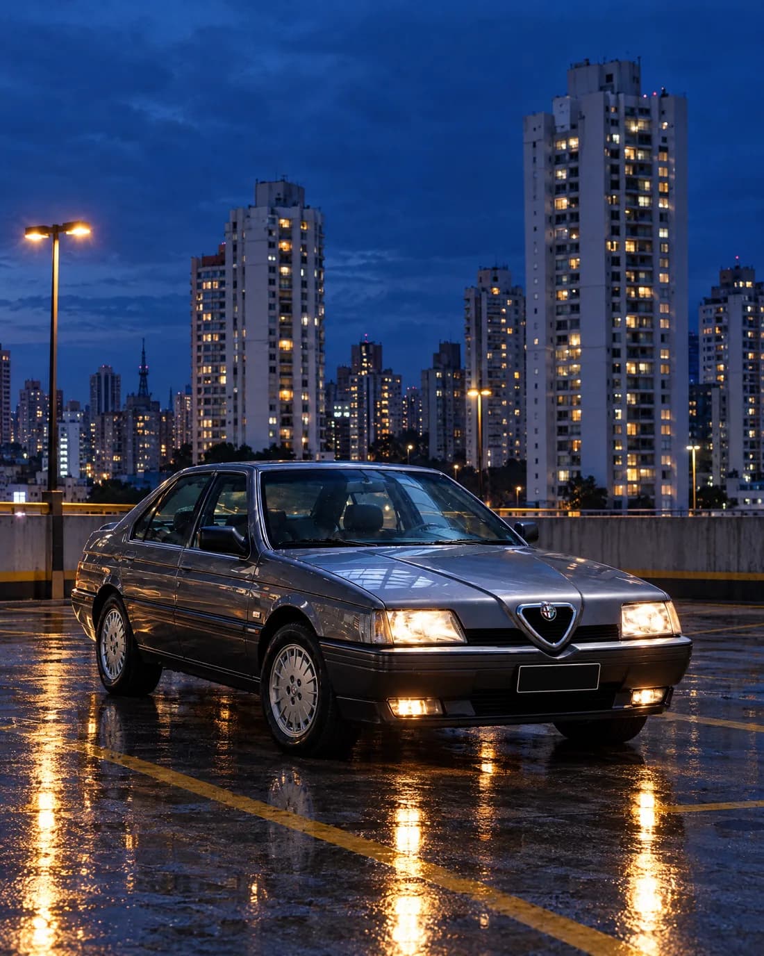 O Alfa Romeo 164 cinza num estacionamento de cobertura em São Paulo, ao anoitecer, com prédios iluminados atrás